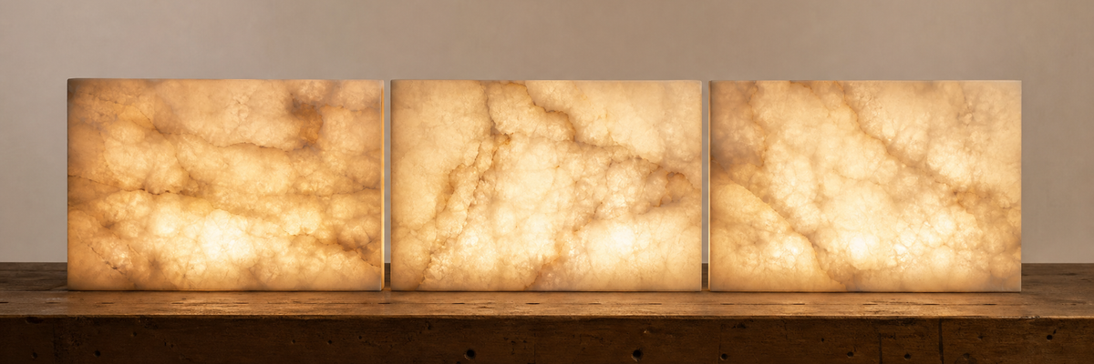 Three backlit slabs of white alabaster glowing amber through their cloudy veining on a workshop bench