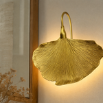 A sculptural metal wall sconce shaped like a ginkgo leaf with a textured gold finish and a curved neck.