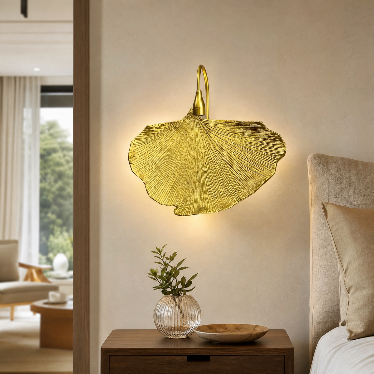 A sculptural metal wall sconce shaped like a ginkgo leaf with a textured gold finish and a curved neck.