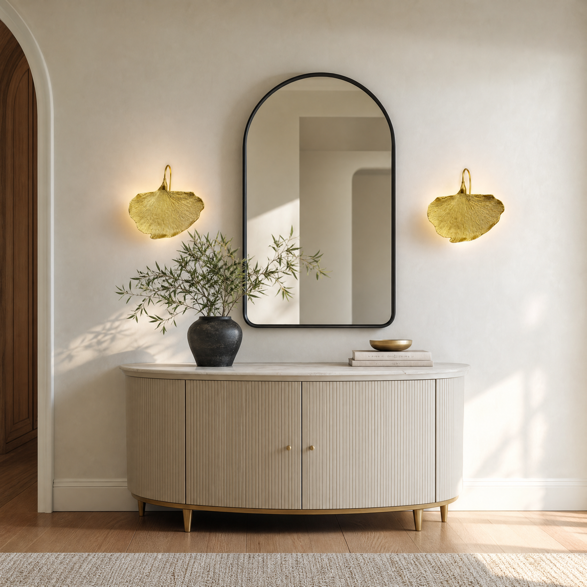 A sculptural metal wall sconce shaped like a ginkgo leaf with a textured gold finish and a curved neck.