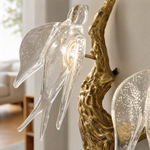 A modern wall sconce with a sculptural, branch-like frame in an antique brass finish and clear textured glass bloom shades.
