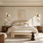 A modern wall sconce with a sculptural, branch-like frame in an antique brass finish and clear textured glass bloom shades.