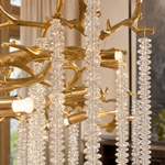 A Yiosi gold metal branch chandelier with cascading crystal beads suspended in a rainfall arrangement.