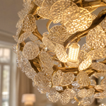 A circular gold metal chandelier with frosted glass leaf accents suspended by thin cables.