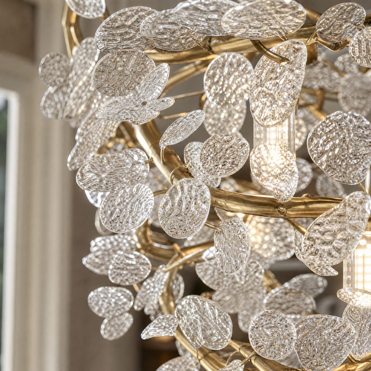 A circular gold metal chandelier with frosted glass leaf accents suspended by thin cables.