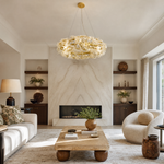 A circular gold metal chandelier with frosted glass leaf accents suspended by thin cables.