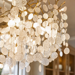 A brass branch chandelier featuring suspended frosted glass leaf elements that provide ambient light.