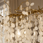 A brass branch chandelier featuring suspended frosted glass leaf elements that provide ambient light.