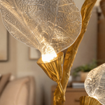 A brass branch-inspired chandelier featuring cascading frosted leaf-shaped glass shades hanging vertically.