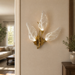 A wall sconce featuring sculpted leaf-shaped textured glass shades and a warm gold metal finish.