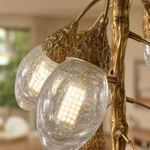 A modern chandelier with an antique brass metal vine frame and glowing glass buds hanging in a bright room.