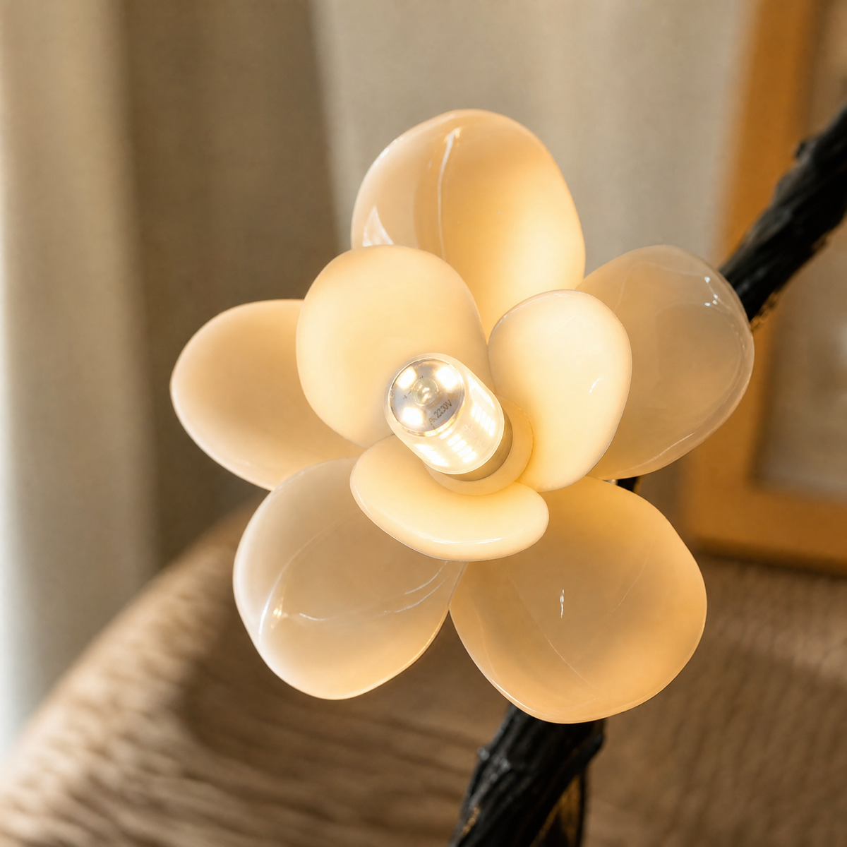 A matte black metal vine branch pendant light with frosted glass floral blossoms suspended from a ceiling mount.