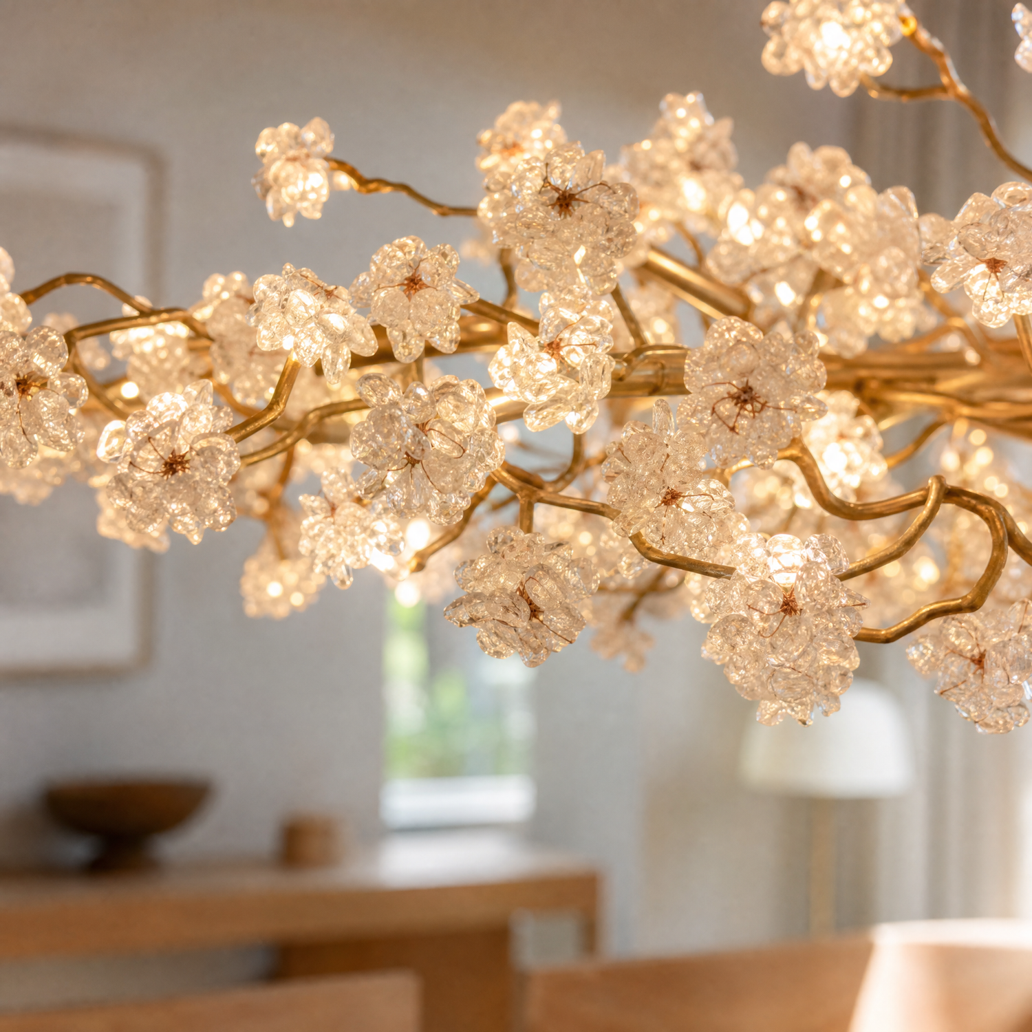 A modern organic chandelier with a warm gold branching frame and textured crystal blossom clusters hangs over a dining table.