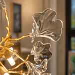 A gold metal branch chandelier with crystal ginkgo leaf shades suspended from a circular canopy.