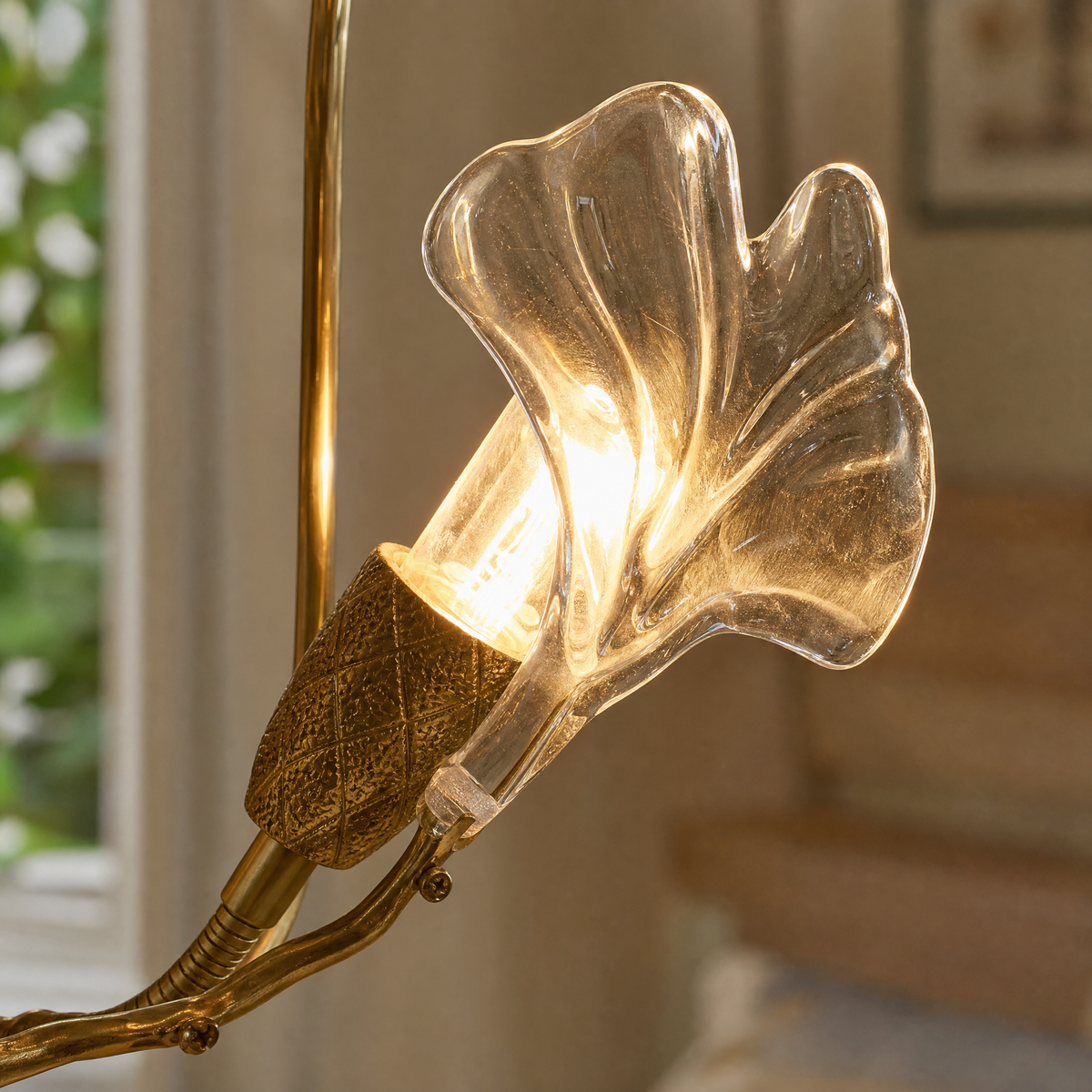A modern wall sconce designed as a sculptural ginkgo branch in a warm brass finish with clear textured glass leaf shades.