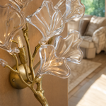 A modern wall sconce designed as a sculptural ginkgo branch in a warm brass finish with clear textured glass leaf shades.