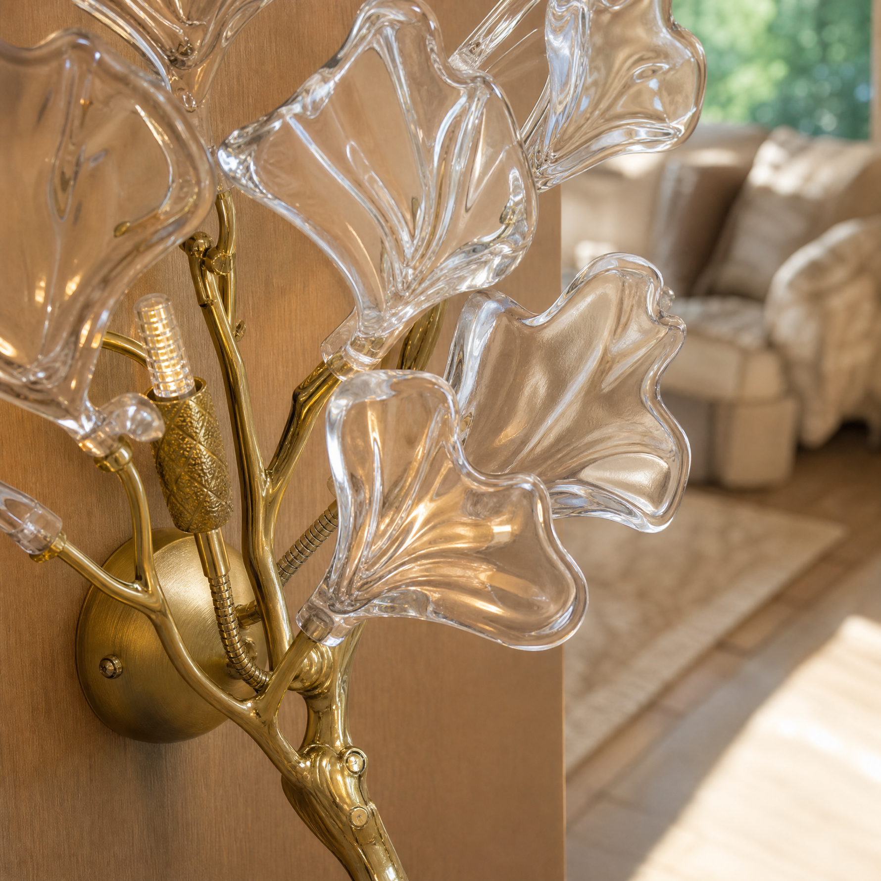 A modern wall sconce designed as a sculptural ginkgo branch in a warm brass finish with clear textured glass leaf shades.