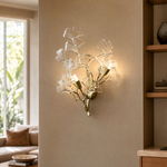 A modern wall sconce designed as a sculptural ginkgo branch in a warm brass finish with clear textured glass leaf shades.