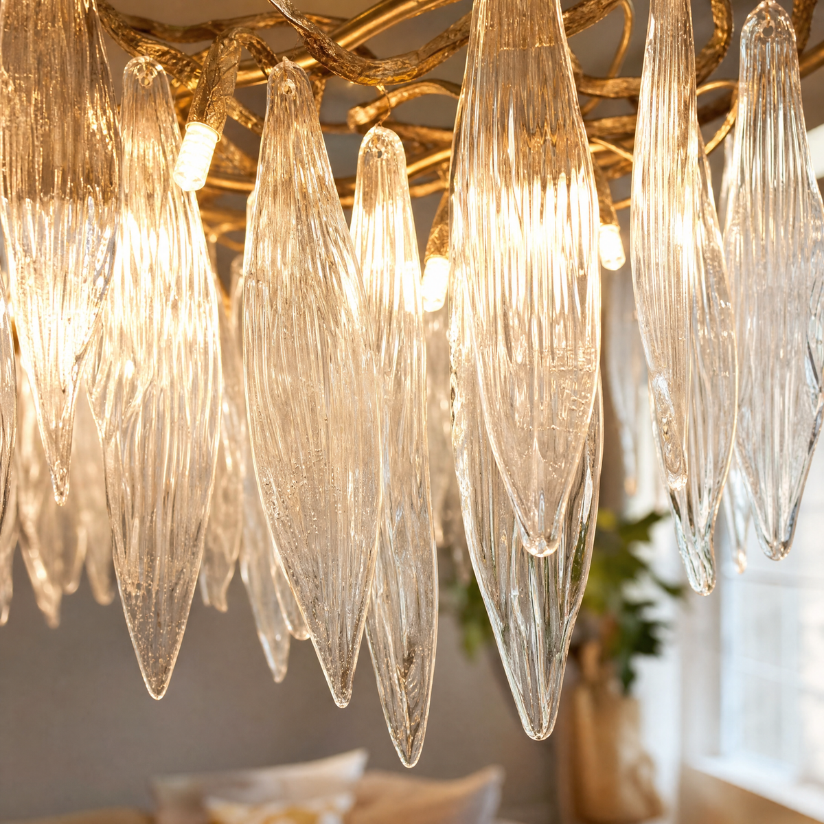 A modern chandelier with elongated textured crystal leaf pendants attached to an antique gold branch-like metal frame.