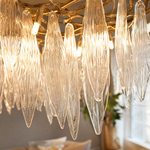 A modern chandelier with elongated textured crystal leaf pendants attached to an antique gold branch-like metal frame.