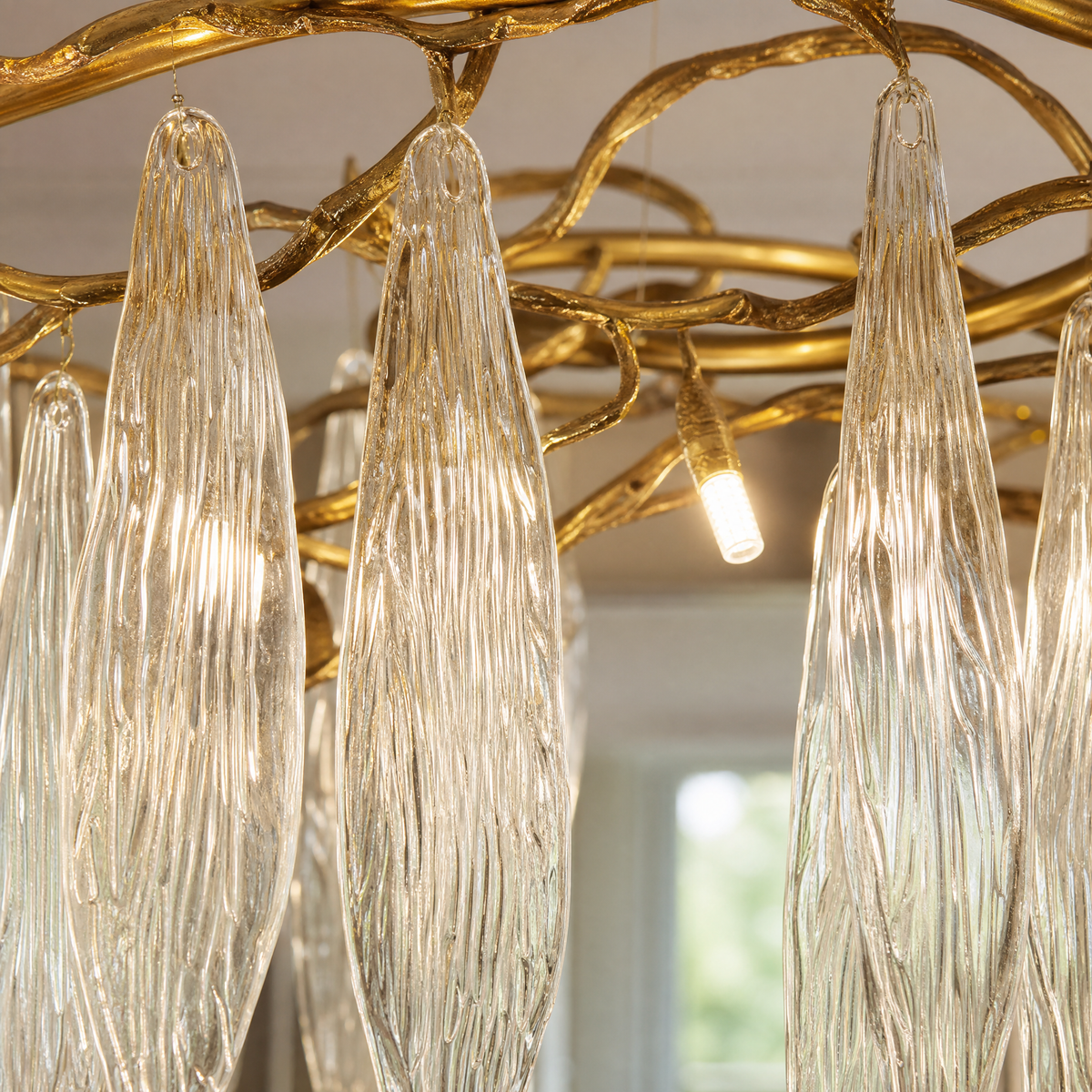 A modern chandelier with elongated textured crystal leaf pendants attached to an antique gold branch-like metal frame.