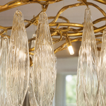 A modern chandelier with elongated textured crystal leaf pendants attached to an antique gold branch-like metal frame.