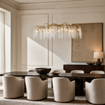 A modern chandelier with elongated textured crystal leaf pendants attached to an antique gold branch-like metal frame.