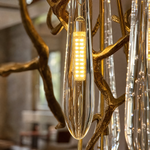 A gold metal branch frame supports a cascading waterfall of clear crystal teardrop prisms in this luxury chandelier.