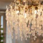 A modern branch chandelier with a gold finish features cascading textured clear glass discs, diffusing a warm ambient light.