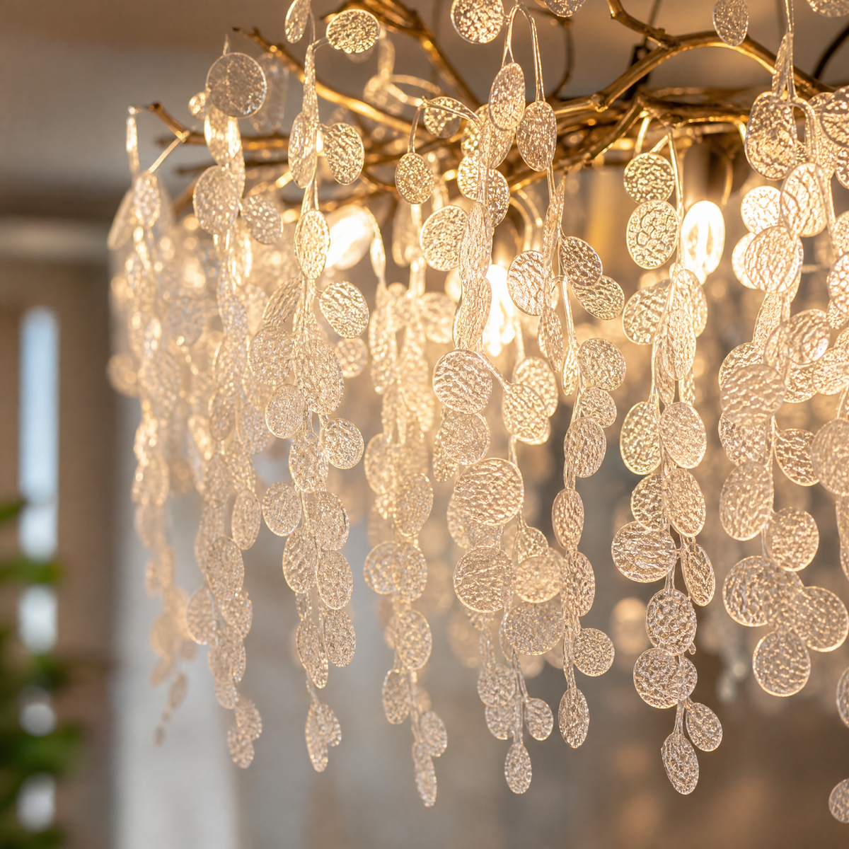 A modern branch chandelier with a gold finish features cascading textured clear glass discs, diffusing a warm ambient light.