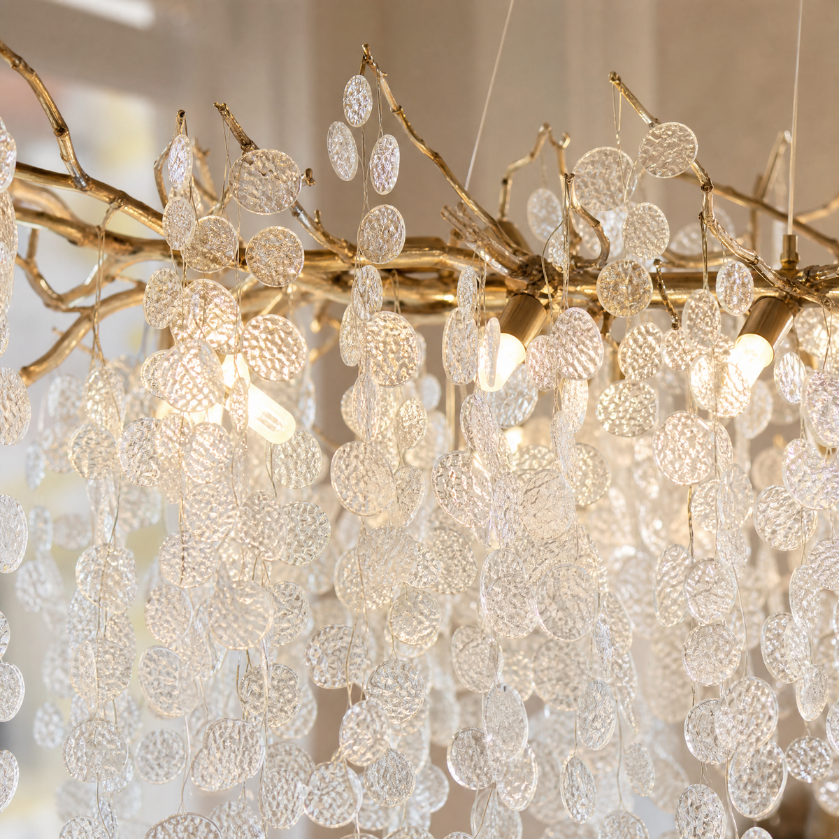 A modern branch chandelier with a gold finish features cascading textured clear glass discs, diffusing a warm ambient light.