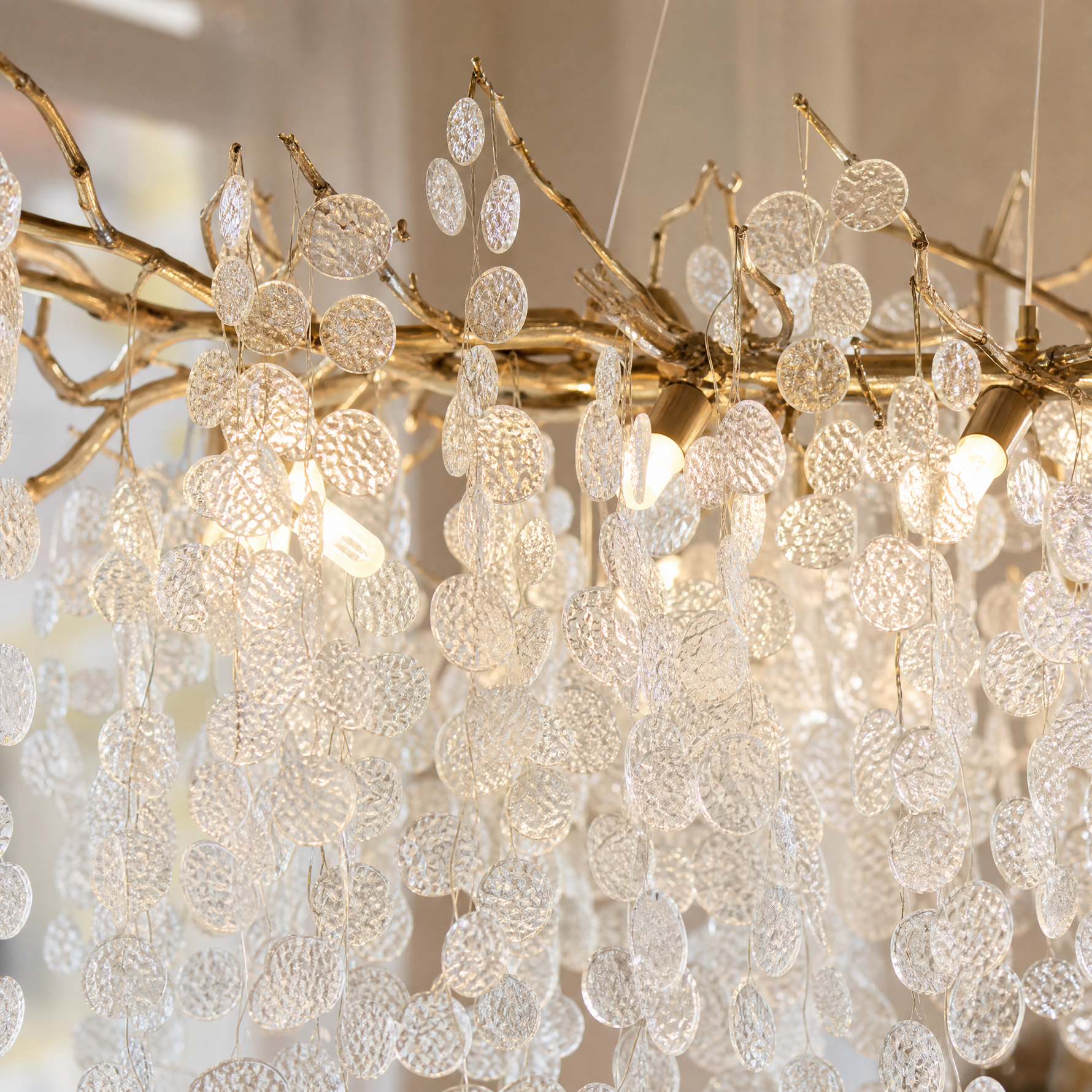 A modern branch chandelier with a gold finish features cascading textured clear glass discs, diffusing a warm ambient light.