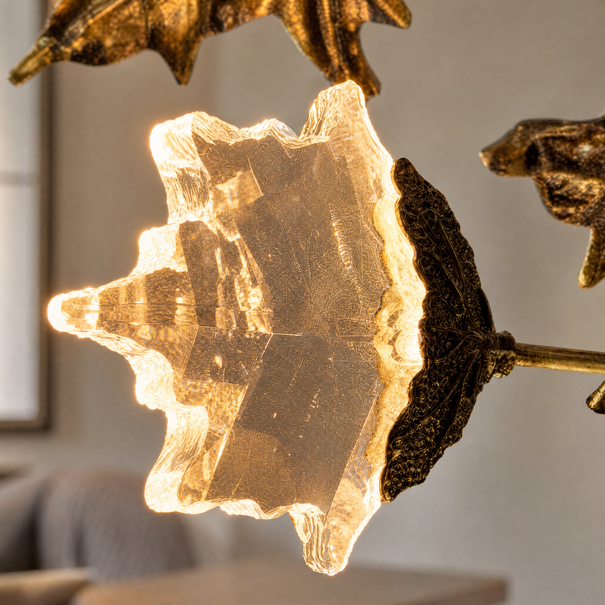 A horizontal, sculptural branch chandelier with a textured antique brass finish and illuminated leaf-shaped crystals.