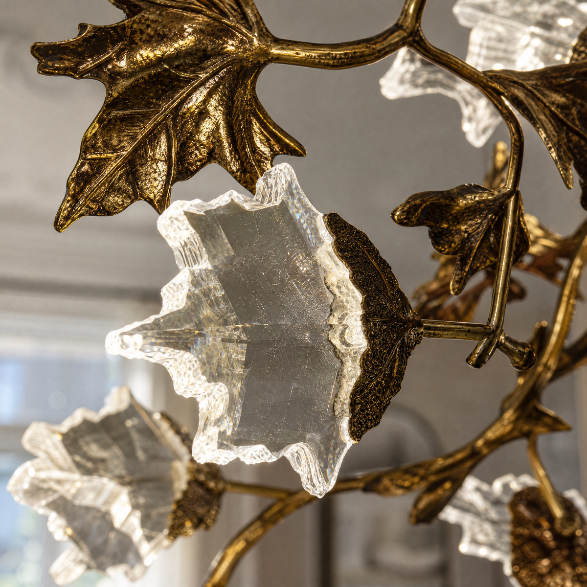 A horizontal, sculptural branch chandelier with a textured antique brass finish and illuminated leaf-shaped crystals.