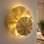 A contemporary wall sconce made of two overlapping metal discs with a textured sunburst pattern in a warm brass finish.