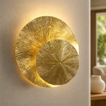 A contemporary wall sconce made of two overlapping metal discs with a textured sunburst pattern in a warm brass finish.