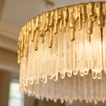 A double-tier chandelier with icicle-style textured crystal drops and a satin warm gold metal band.