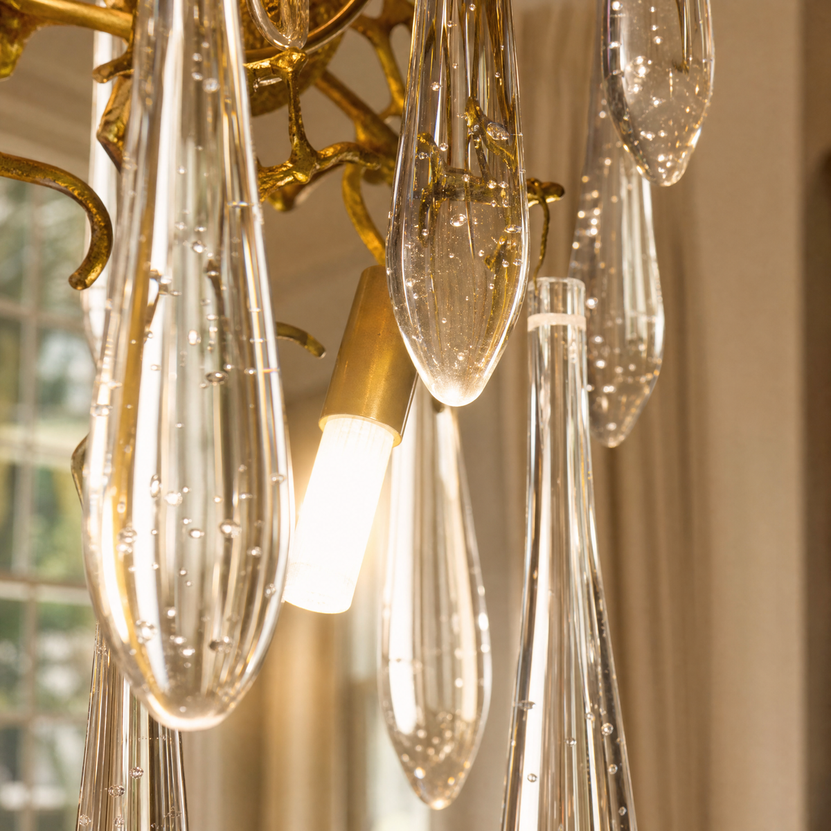 A wall sconce featuring an antique brass branch-inspired metal frame with hanging clear crystal icicle drops.