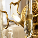 A wall sconce featuring an antique brass branch-inspired metal frame with hanging clear crystal icicle drops.