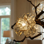An antique brass chandelier with branching arms and frosted glass blossom shades suspended by cables.