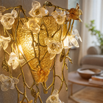 A gold metal wall sconce features a floral vine design with amber glass accents mounted on a wall.