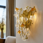 A gold metal wall sconce features a floral vine design with amber glass accents mounted on a wall.