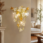 A gold metal wall sconce features a floral vine design with amber glass accents mounted on a wall.