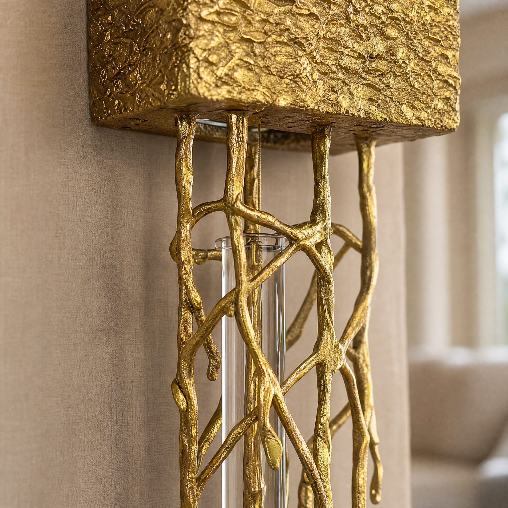 A contemporary wall sconce with a sculptural gilded gold branch frame and a single vertical crystal drop on a rectangular