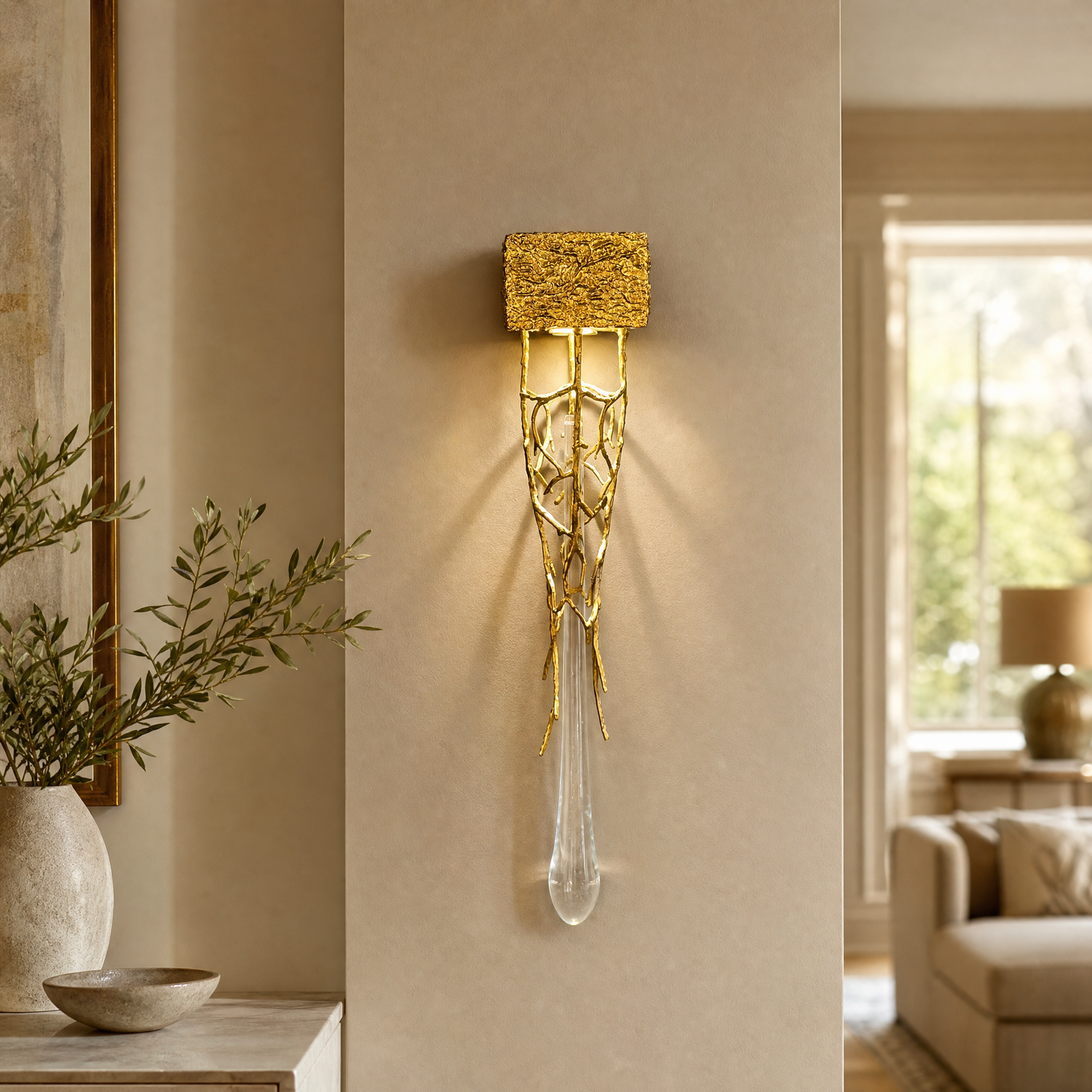 A contemporary wall sconce with a sculptural gilded gold branch frame and a single vertical crystal drop on a rectangular
