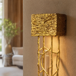 A contemporary wall sconce with a sculptural gilded gold branch frame and a single vertical crystal drop on a rectangular
