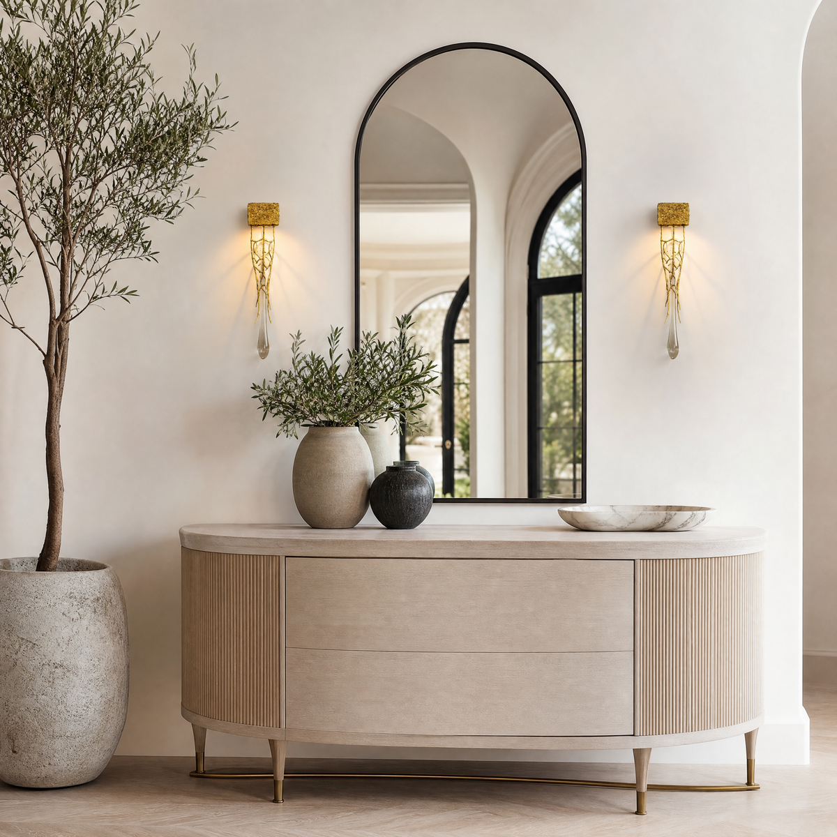 A contemporary wall sconce with a sculptural gilded gold branch frame and a single vertical crystal drop on a rectangular