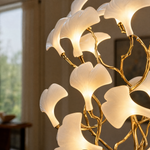 A wall sconce featuring white ceramic ginkgo leaf shades attached to a polished brass metal frame.