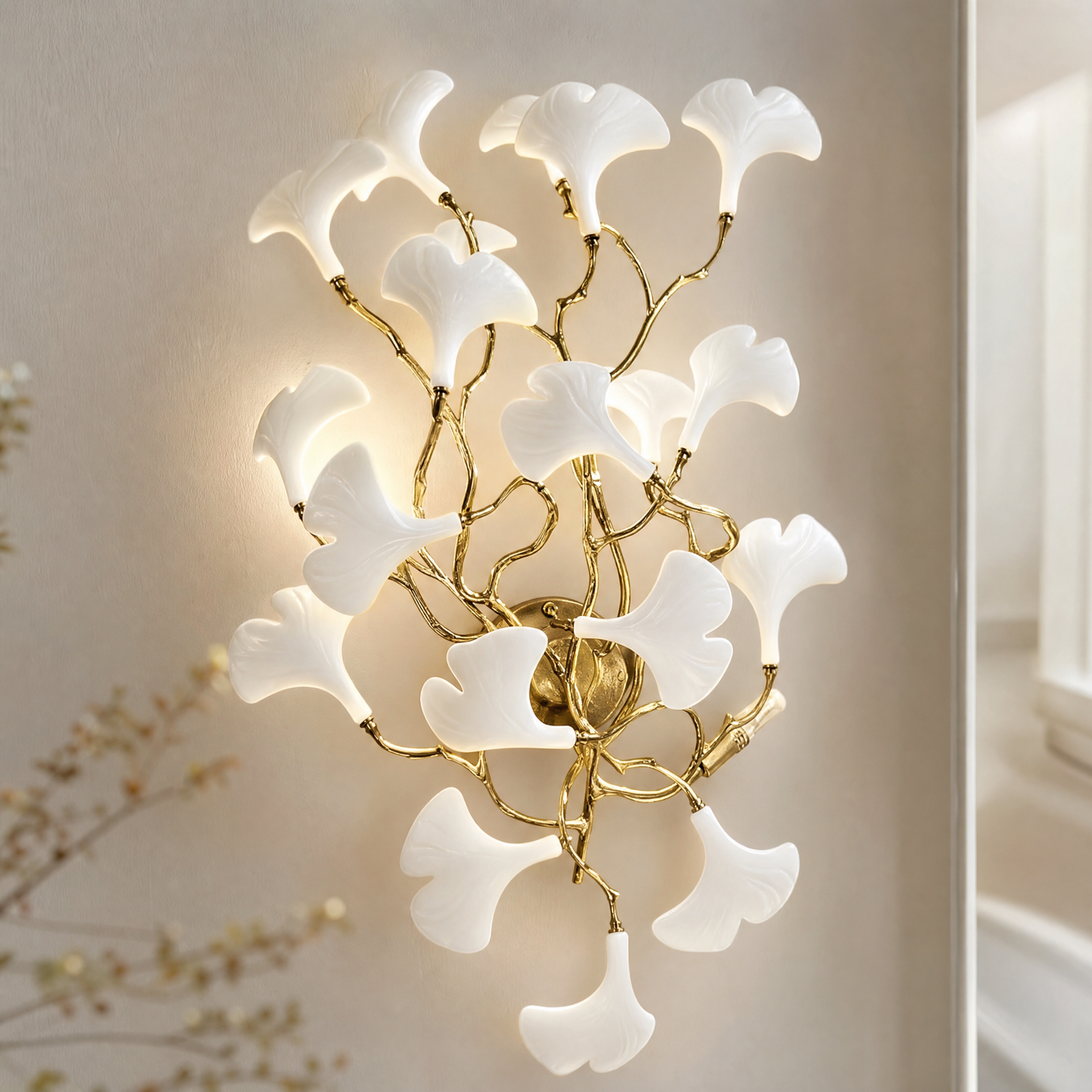 A wall sconce featuring white ceramic ginkgo leaf shades attached to a polished brass metal frame.