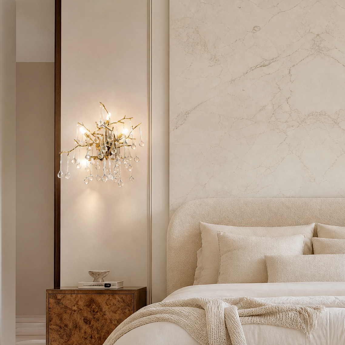 A wall sconce featuring a gold branch-shaped metal frame decorated with hanging teardrop crystal accents.